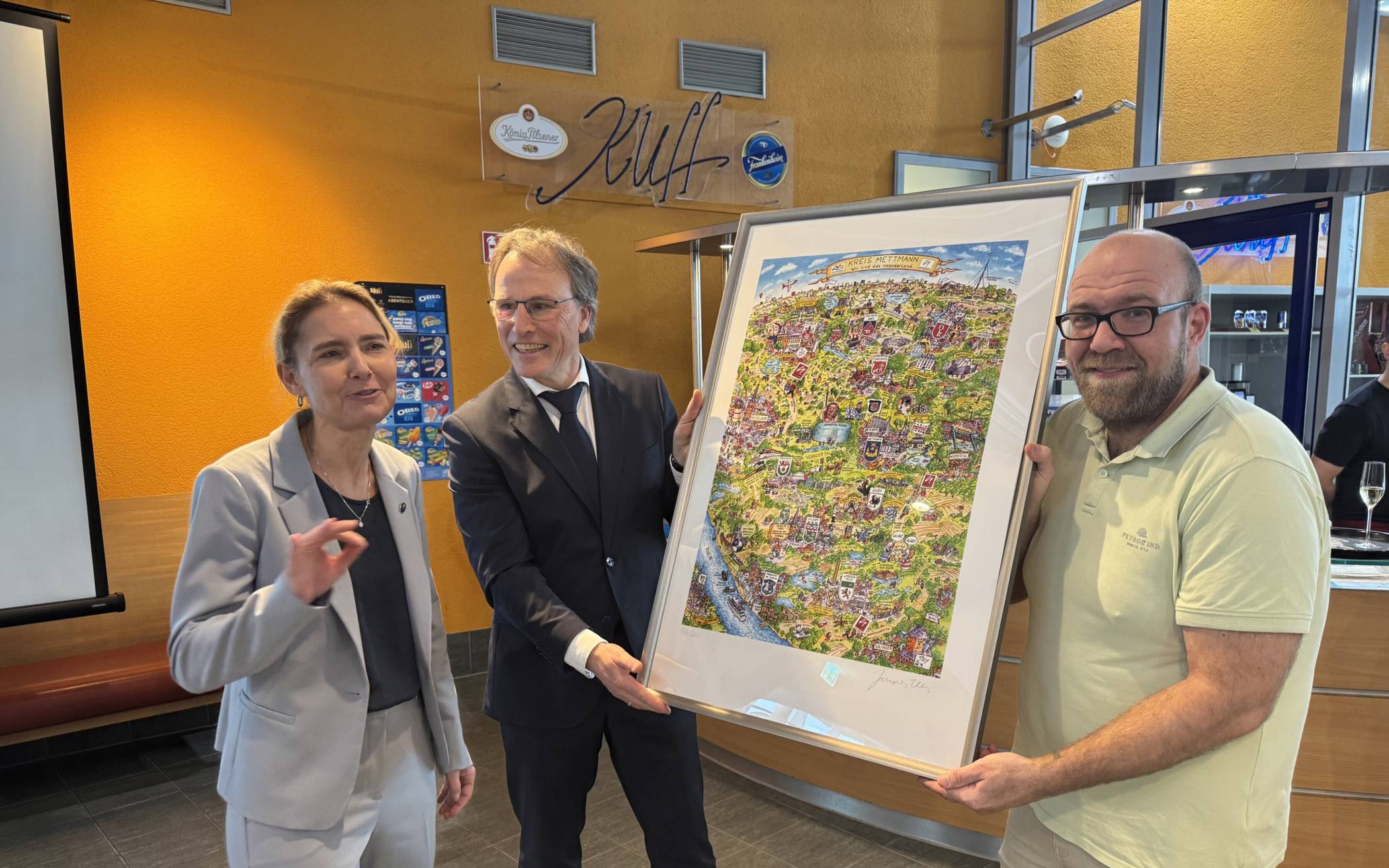  Landrätin Dr. Bettina Warnecke schenkte den Vertretern des Neanderbades, Gregor Jeken (Stadtwerke-Chef, Mitte) und Kevin Bechmann (Leiter des Neanderbades) zum 20. Geburtstag ein Wimmelbild von Jacques Tilly. 