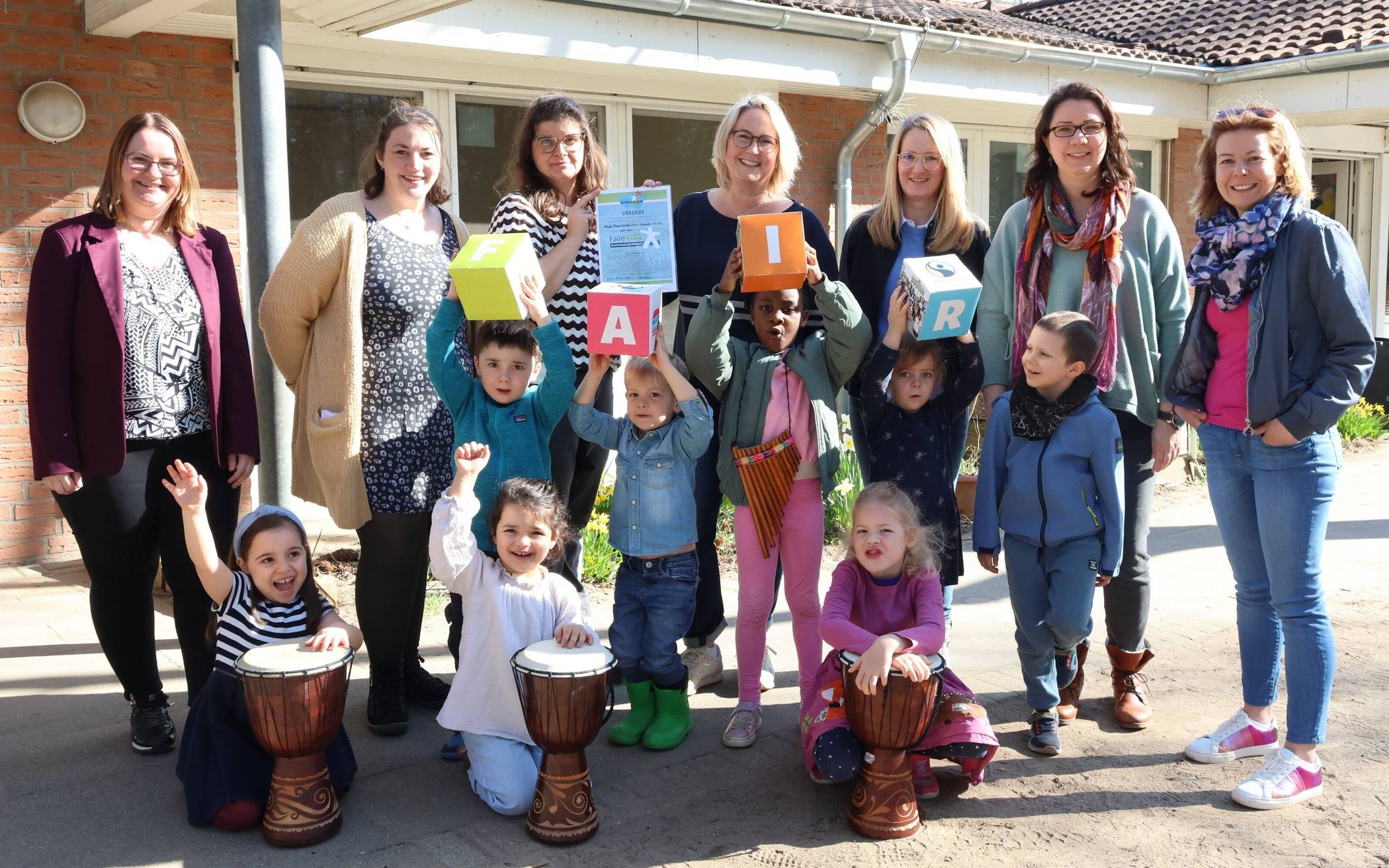  Kita-Leiterin Minka Looschen (hinten, 3. v. l.) freut sich mit den Kita-Kindern, den Eltern und dem Team des Familienzentrums Hochdahl-Mitte über die erneute Zertifizierung als FaireKITA. Sandra Preußer, Leiterin des Fachbereichs Umwelt · Klimaschutz (1.v.l.) und Stephanie Rüberg, Leiterin der Abteilung Kindertagesbetreuung der Stadt Erkrath (3. v. r.), feierten mit.  